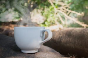 Big white cup coffee or hot drink on the rock under tree shade and happy morning fresh nature forest background woth copy space